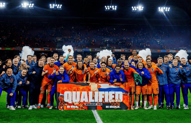 Group of Netherlands players celebrate on a soccer field, holding a banner that reads 'Qualified' after qualifying for World Cup 2026.