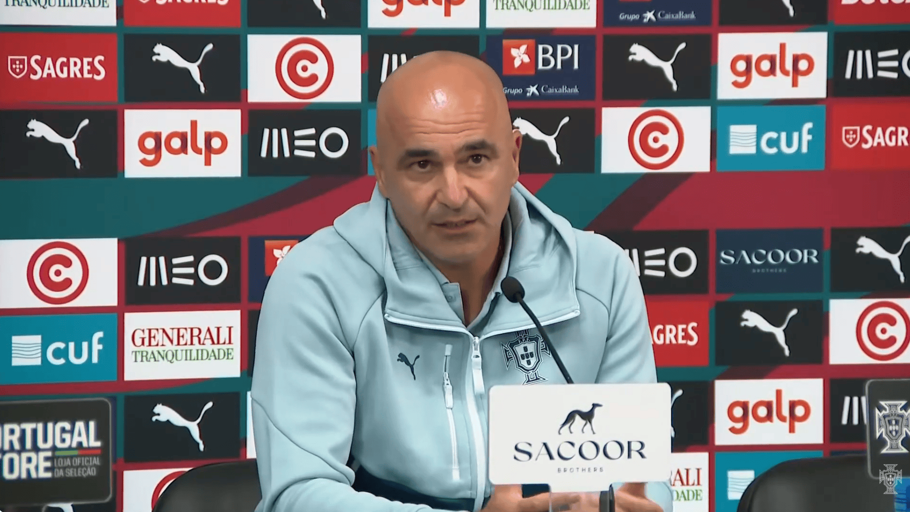 hupu-football-1780701705248-kaiyun-1png - 开云体育中心 Bald man in a light-blue zip jacket speaks at a press conference, microphone in front, sponsor logos behind him.