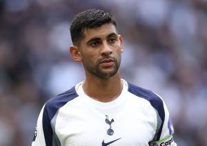 Soccer player in a white and navy jersey with a captain's armband, looking off to the side on the field.