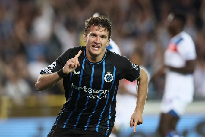 Belgian footballer in Club Brugge kit celebrating a goal, pointing with his right hand on the field.
